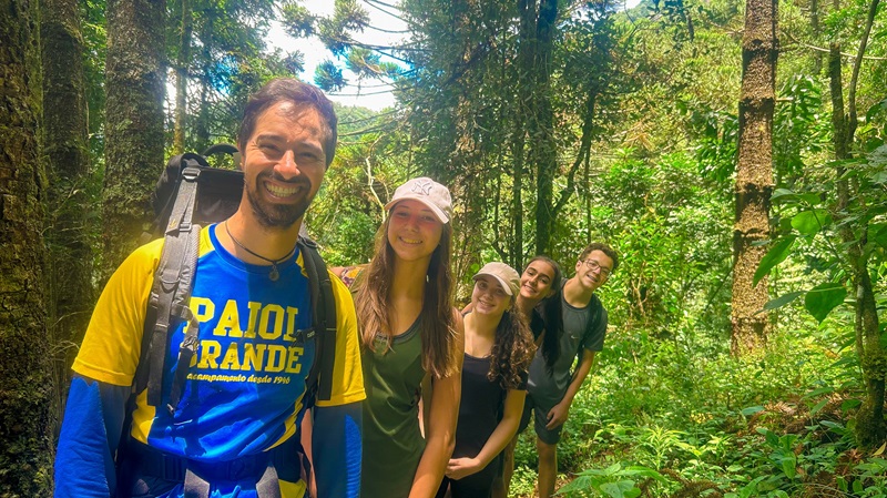 monitos e crianças posam em uma trilha na mata, todos sorriem e faz sol. 