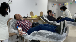 dois homens doando sangue nas macas do bando de sangue, um oriental e um ruivo de barba.