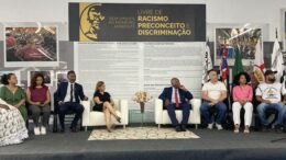 convidados sentados em um pequeno palco para a Cerimônia de lançamento do Colégio Técnico Dandara dos Palmares