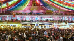 multidão na festa junina, e no teto faixas coloridas enfeitam o local