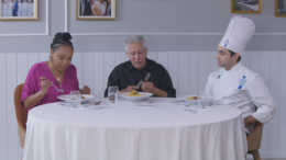 Os jurados do programa, Larissa Januário, Tavinho Ceschi e Vitor Oliveira sentados à mesa, provando algum dos pratos.