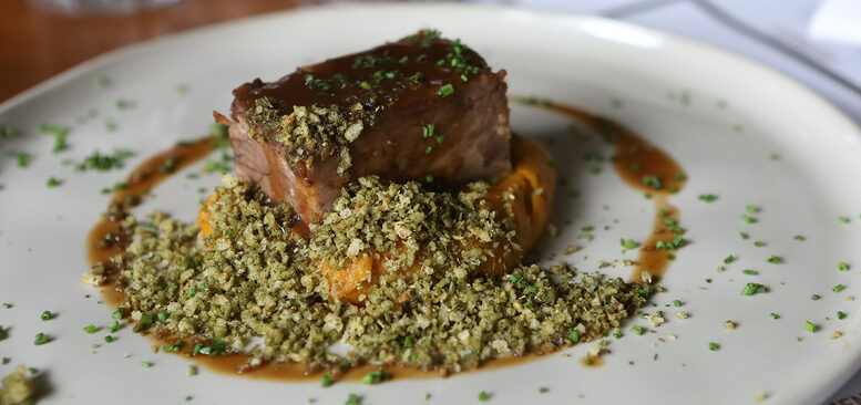 prato com um pedaço de costela, com um pouco de molho e uma farofa verde