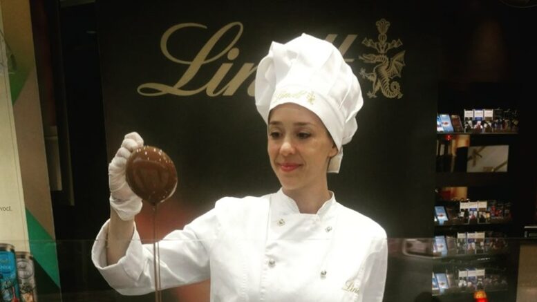 imagem de chef com chapeu e avental, sorrindo, olhando para uma concha que ela segura, derramando chocolate derretido.