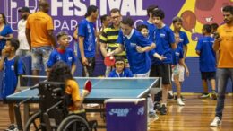 imagem de edição anterior do festival, com duas crianças jogando tenis de mesa, uma cadeirante e outro em pé, e vários outros ao redor.