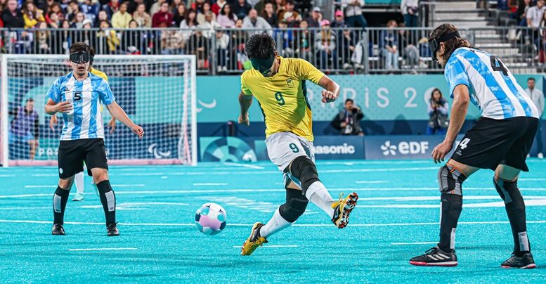 imagem de jogo de futebol de cegos, com dois argentinos um de cada lado e ao centro um vbrasileiro chutando a bola