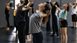 grupo de bailarinos em roupas normais de ginástica, de braços abertos e para trás.