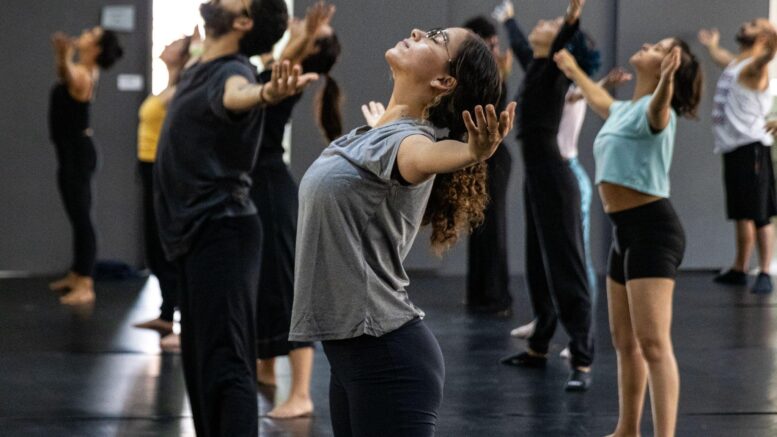 grupo de bailarinos em roupas normais de ginástica, de braços abertos e para trás.