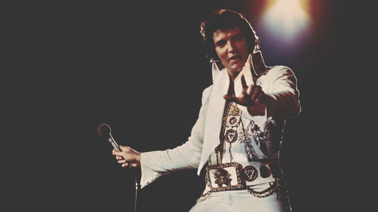 elviz presley vestido de branco com uma jaqueta aberta em um show