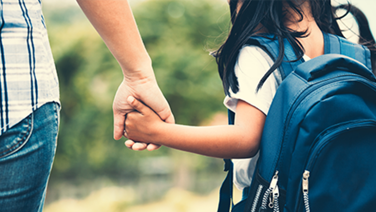 imagem fechada de um adulto de mão dada com uma menina com mochila escolar, ambos de costas, imagem fechada nas mãos e no ombro da menina