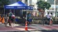 tenda azul montada na praça do ciclista,, com uma bike erguida no equipamento e dois ciclistas aguardando sua vez.