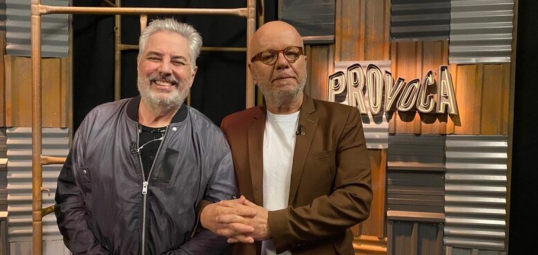 roberto de carvlaho, cabelo e barba branca, em pé, de braço dado com Marcelo Tas, calvo e de óculos, em frente ao ccenário do programa com a logo Provoca, na parede.