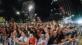 imagem de publico vibrando junto à grade de proteção de algum show ao ar livre à noite.