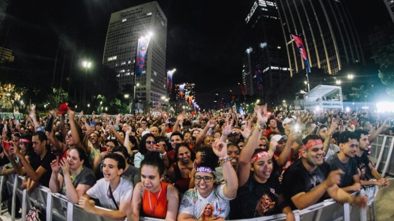 imagem de publico vibrando junto à grade de proteção de algum show ao ar livre à noite.