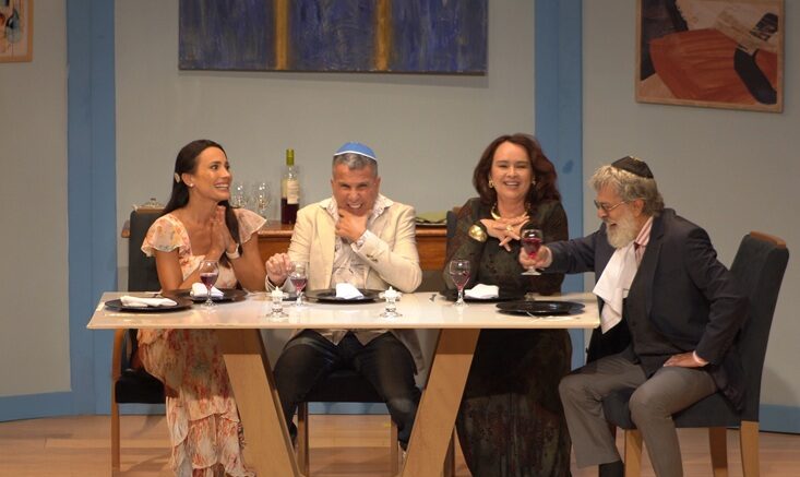 quatro atores sentados em uma mesa e rindo.