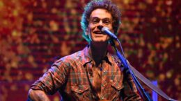 imagem de nando Reis fechada, ele tocando violão e cantando no microfone, olhando apra a camera