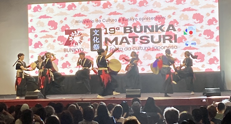 apresentação de taiko em um palco com um telação mostrando que é o 19º Bunka Matsuri