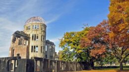 imagem de um pre´dio em ruínas.a lado de árvores com grandes copas e um céu azul