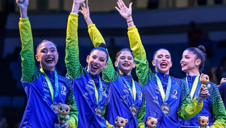 Pódio com equipe brasileira de ginastica ritmica, com a medalha de prata e o mascotinho da competição nas mãos