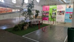 imagem da simulação de uma vaga verde com tatepe te grama, banco e plantas, ao lado de uma simulação de vaga de carro, com piso cinza e paineis ao fundo.