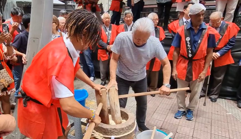 um jovem e um senhor de idade com maretelos de madeira socando arroz em um pilão.