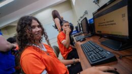 dois jovens sentados em frente a computadores em um local de acesso publico do governo federal