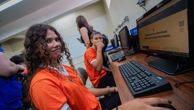 dois jovens sentados em frente a computadores em um local de acesso publico do governo federal