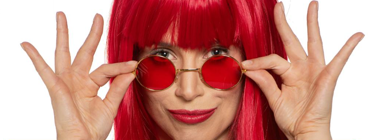 Mel Lisboa em close com figurino de Rita Lee, segurando óculos rodondos..