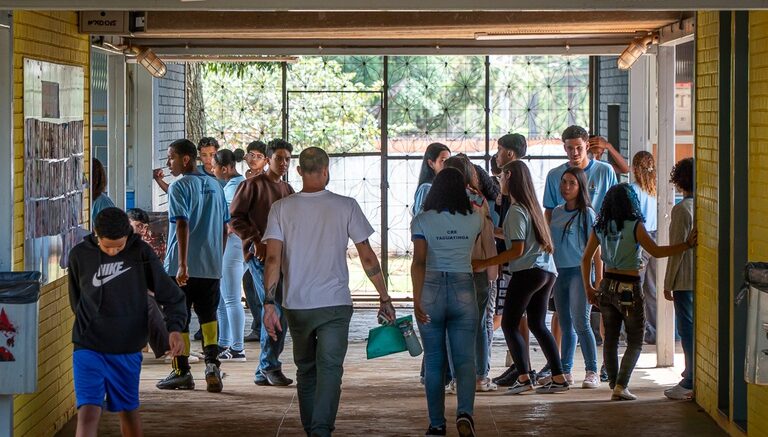 alunos de ensino médio de escola publica, em um corredor largo com janelão atrás