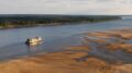 imagem gerada por IA mostra um barco navegando uma lateral de um largo rio com a outra faixa bastante assoreada, com bancos de terra