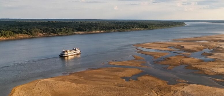 imagem gerada por IA mostra um barco navegando uma lateral de um largo rio com a outra faixa bastante assoreada, com bancos de terra