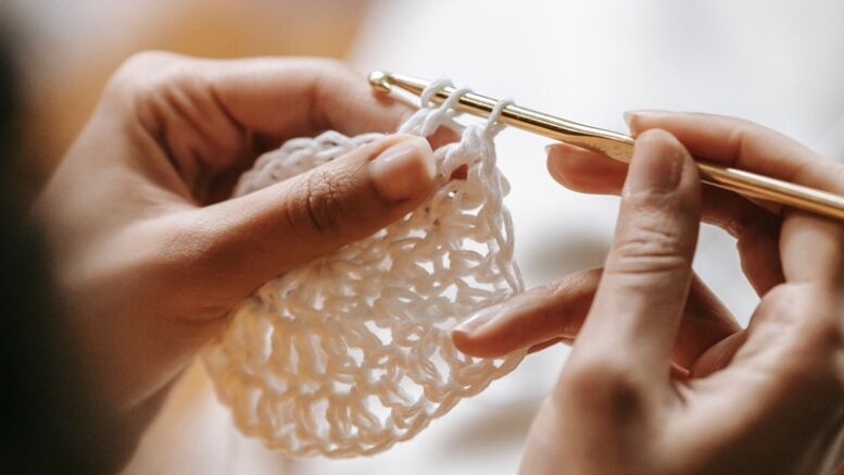 mãos de mulher fazendo um quadrado branco de croche com uma agulha dourada