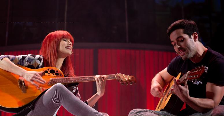 imagem de Mel Lisboa como Rita Lee, tocando violão ao lado do ator Bruno Fraga, como Roberto de Carvalho, também ao violão.