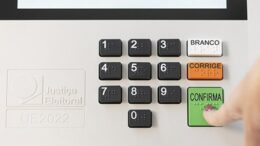 imagem do teclado da urna eletrônica com dedo feminino apertando a tecla 'confirma'.