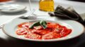 imagem de prato de ravioli com molho vermelho, em uma mesa posta.
