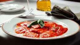 imagem de prato de ravioli com molho vermelho, em uma mesa posta.