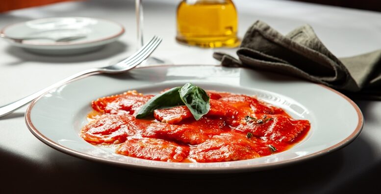 imagem de prato de ravioli com molho vermelho, em uma mesa posta.