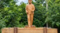 estátua de um menino com duas romãs nas mãos e algumas a seus pés. ao fundo arvores verdadeiras de romã.