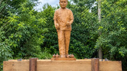 estátua de um menino com duas romãs nas mãos e algumas a seus pés. ao fundo arvores verdadeiras de romã.